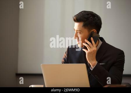 Young businessman talking on mobile phone while using laptop Stock Photo