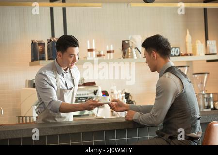 Young waiter offers businessman a cup of coffee Stock Photo