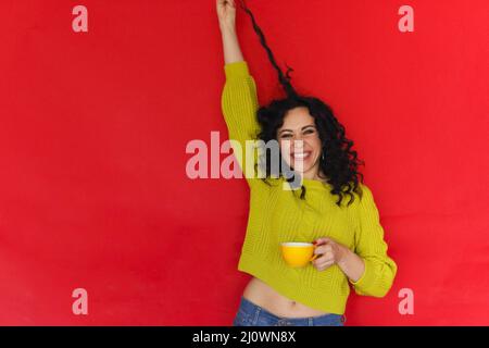 Happy overjoyed young woman with tea cup in hands playing with her curly hair and smiling Stock Photo