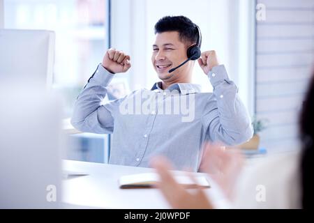 Another big sale made by me. Shot of a young call centre agent cheering while working on a computer in an office. Stock Photo
