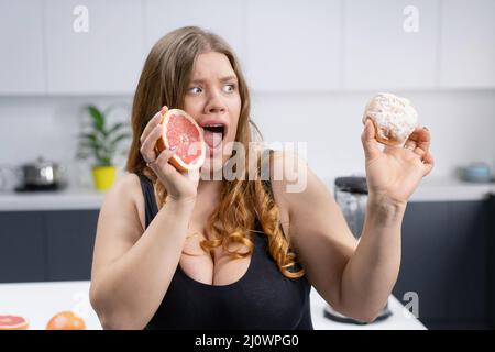 Concept of healthy eating, body care. Lovely girl makes a choice between sugar and fruit. Tasty vitamins. Weight loss, detox, bo Stock Photo