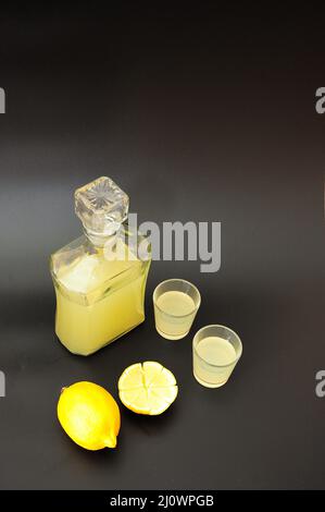 Limoncello, a traditional Italian liqueur in a bottle and two glasses on a black background and a ripe citrus next to it. Close-up. Stock Photo