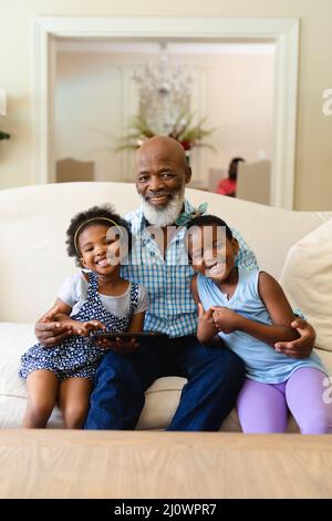 African american grandfather and two granddaughters with digital tablet smiling at home Stock Photo