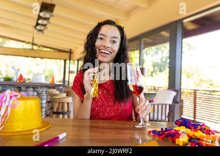 Portrait of happy biracial young woman with champagne flute enjoying party on video call Stock Photo