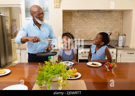 African american grandfather serving breakfast for his two granddaughters in the kitchen at home Stock Photo