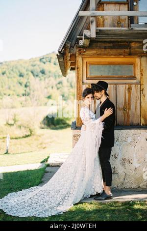 Groom hugs bride near the wall of a house. Side view Stock Photo