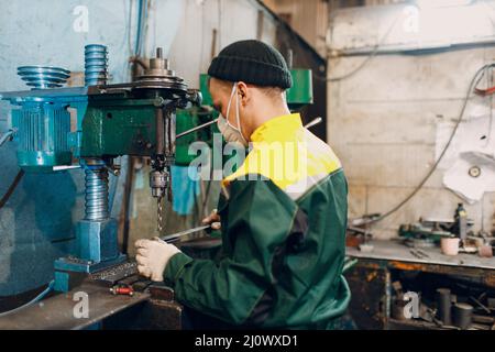 Worker with drilling boring machine works on metal factory Stock Photo