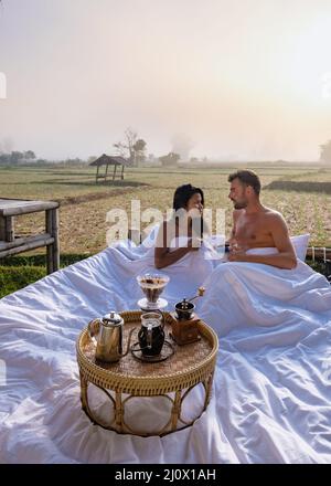 Sunrise over rice paddies in Nan Thailand, man and woman in outdoor bed waking up with coffee in the morning in Thailand Nan Stock Photo