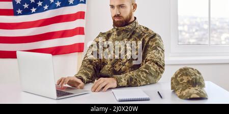 Young soldier who serves in US army sitting in office and working on laptop computer Stock Photo
