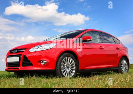 Red car on a blue sky background with white clouds. The car is standing in the field on the green grass. Stock Photo