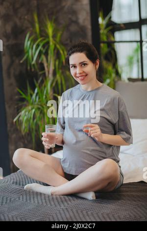 Pregnant woman taking prenatal vitamins during pregnancy, holding water glass and pill in hands Stock Photo