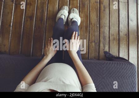 Woman putting on soft plush warm slippers while sitting on sofa at cozy home in cold season. Top view Stock Photo