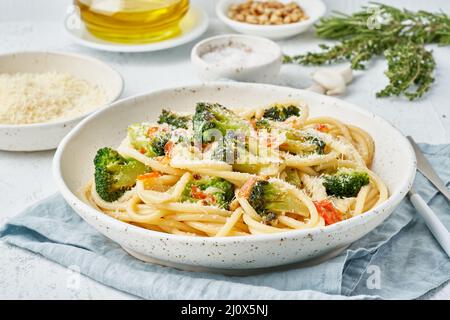 Spaghetti pasta with broccoli, bucatini with peppers, garlic, pine nuts. Light white table. Stock Photo
