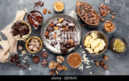 Chocolate bar, crushed dark chocolate pieces, cocoa beans, cocoa butter, nuts, top view on dark background. Stock Photo