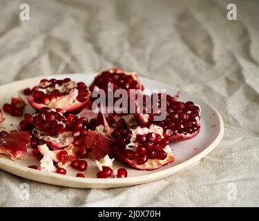 Still life with broken open pomegranate and seeds on plate on table covered with crumpled beige tablecloth Stock Photo