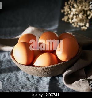 Unusual Easter on dark background. Bowl of brown eggs on dark blue table, flowers. Stock Photo