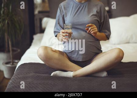 Pregnant woman taking prenatal vitamins during pregnancy, holding water glass and pill in her hands Stock Photo