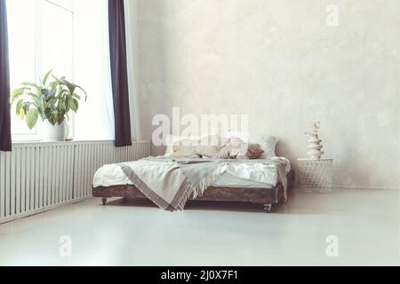Stylish minimalist loft style bedroom interior with light concrete walls, king size wooden bed with pillows Stock Photo