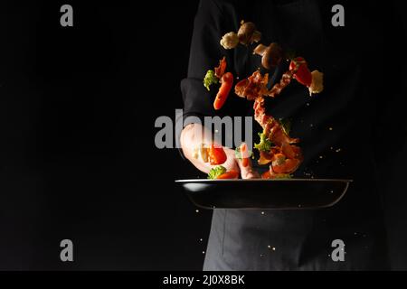 Cook preparing bacon slices with garlic and hot pepper and broccoli in a pan, freezing in the air, on a black background, recipe book, menu, gastronom Stock Photo