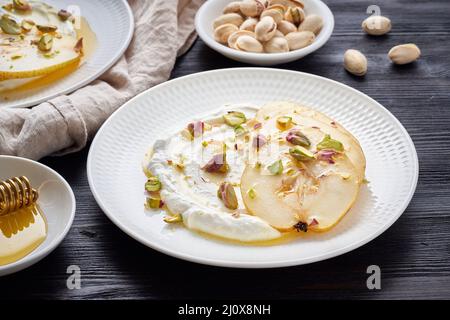 Ricotta with pears, pistachios and honey or maple syrup on two white plate on dark Stock Photo