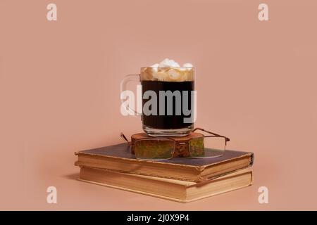 A glass cup of coffee with marshmallows and glasses on a stack of old books Stock Photo
