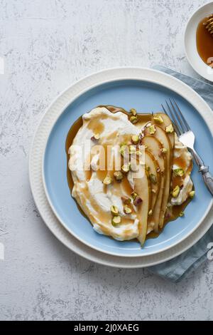 Ricotta with pears, pistachios and honey or maple syrup on blue plate on white table. Stock Photo
