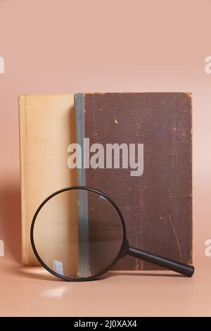 A stack of old battered books and a magnifying glass Stock Photo