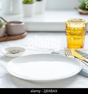 Side view of clean empty white plate, glass of water, fork and knife on white tablecloth Stock Photo