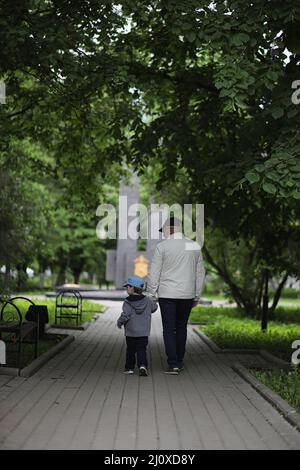 Grandpa is walking with her grandson in a spring park. Grandson and grandfather on walk. Grandpa is talking to a little boy. Stock Photo