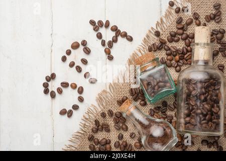 A grain of coffee in a glass jar, and the inscription with a spoon of grain on a light wooden texture. Stock Photo