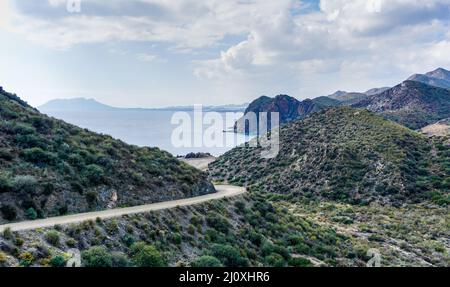 Curvy dirt road leading down to a secluded beach on a wild and mountainous coastline Stock Photo