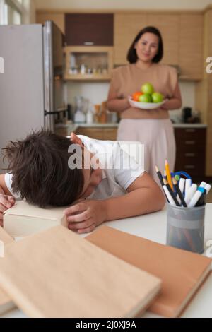 Mother carrying bowl of fruits to little son fell asleep after studying at home for many hours Stock Photo