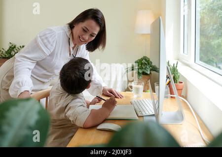 Smiling mother checking on her son studying from home due to coronavirus pandemic Stock Photo