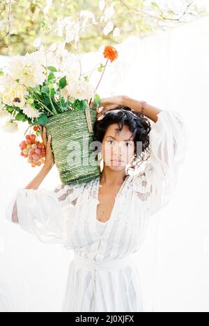 Woman standing in the garden with a basket of flowers on her shoulder Stock Photo
