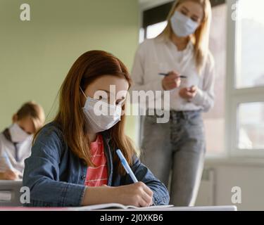 Children with medical masks learning school with female teacher Stock Photo