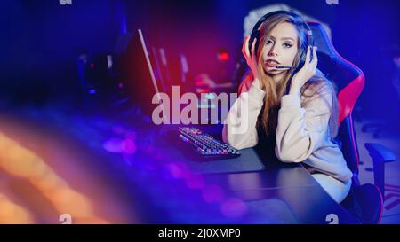 Portrait young woman happy pro gamer having live stream and playing in online video game to subscribers, blue neon color. Stock Photo