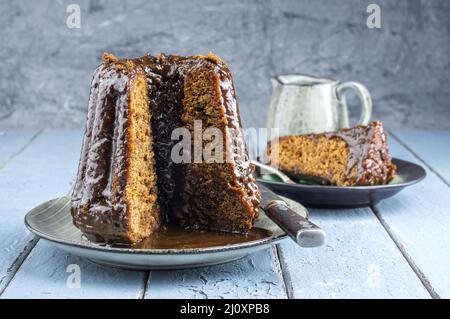 Traditional English sticky toffee pudding with caramel glaze served as close-up on a design plate Stock Photo