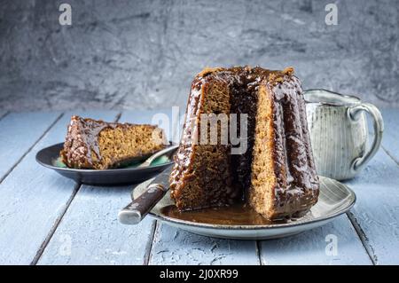Traditional English sticky toffee pudding with caramel glaze served as close-up on a design plate Stock Photo