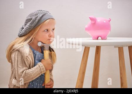 To break or not to break. A cute girl with a hammer eyeing her piggy bank. Stock Photo