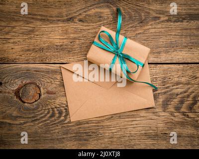 Holiday gift box, tied with green ribbon, envelope of Kraft paper, blank on the wooden weathered rustic background, top view. Stock Photo