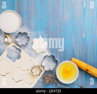 https://l450v.alamy.com/450v/2j0xtjd/raw-puff-pastry-dough-lies-on-a-blue-wooden-table-sprinkled-with-flour-figures-for-baking-cut-metal-mold-sugar-and-egg-in-bow-2j0xtjd.jpg