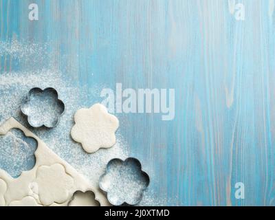 Raw puff pastry dough lies on a blue wooden table, sprinkled with flour. Figures for baking cut metal mold Stock Photo