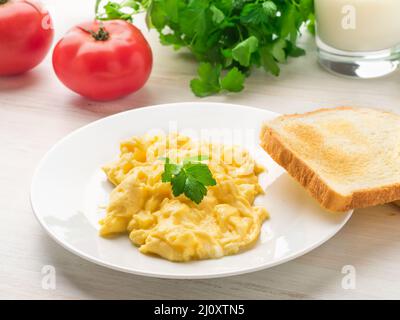 White plate with pan-fried scrambled eggs on a white light background with tomatoes. Omelette, side view Stock Photo