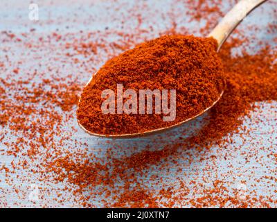 One heaping scoop of spices of paprika, powder scattered on the wooden blue bright light color table, close up, side view Stock Photo