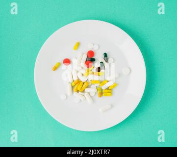 Handful of scattered medicines, pills and tablets on white plate on blue background Stock Photo