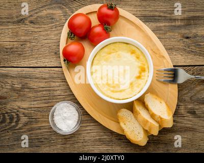 Wood plate with oven-baked omelet of eggs and milk, with tomatoes and toast on brown rustic wooden table, top view