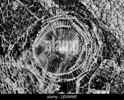 Broken glass. Round hole with radial cracks in the glass. Round white cracks in glass on black background Stock Photo