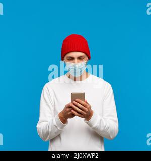 Portrait of man with medical protective face mask, texting on mobile phone. Male write message Stock Photo