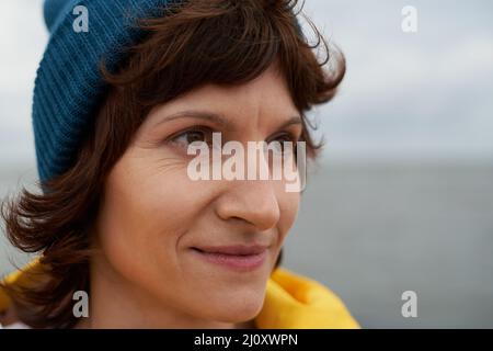 Crop closeup portrait of mature beautiful woman looking away in bright yellow raincoat and blue hat Stock Photo