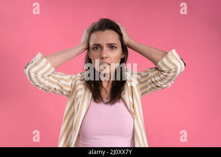 Stressed or having a headache businesswoman in suit holding her head with eyes shut isolated on pink background. Stressed employ